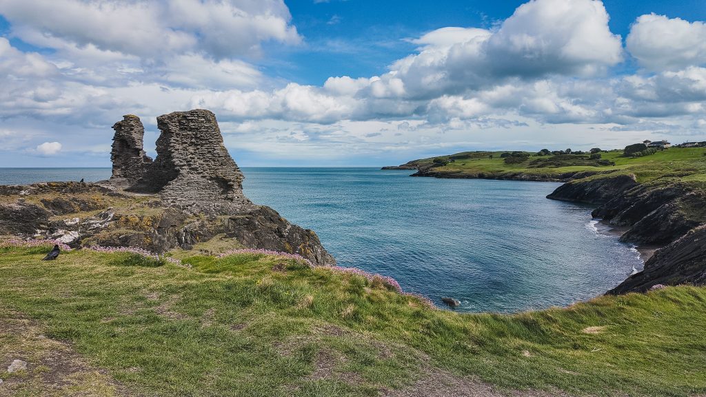 Ruins of a stone castle on a green cliff overlooking turquoise sea in Wicklow, Ireland.