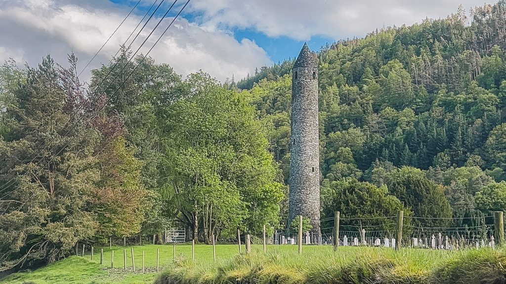 Tall Round Tower surrounded by a green forest in Glendalough Ireland.