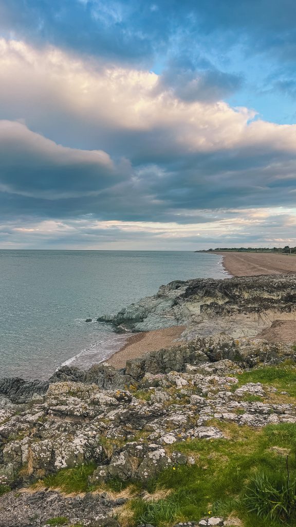 Rocky coastline with sandy coves and turquoise blue water under a cloudy sky in Greystones, Ireland.