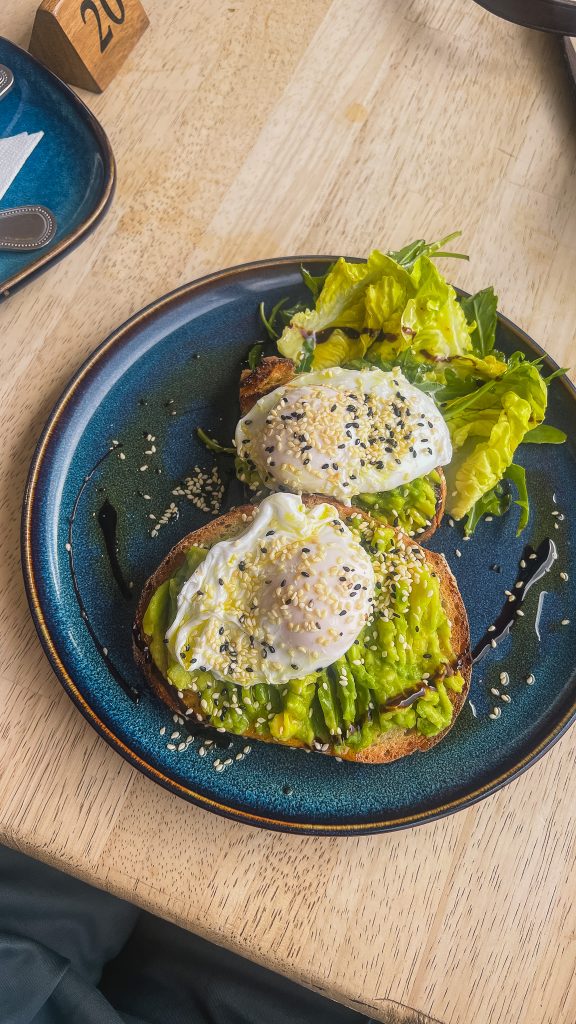 Two slices of avocado toast with egg on it on a blue plate.