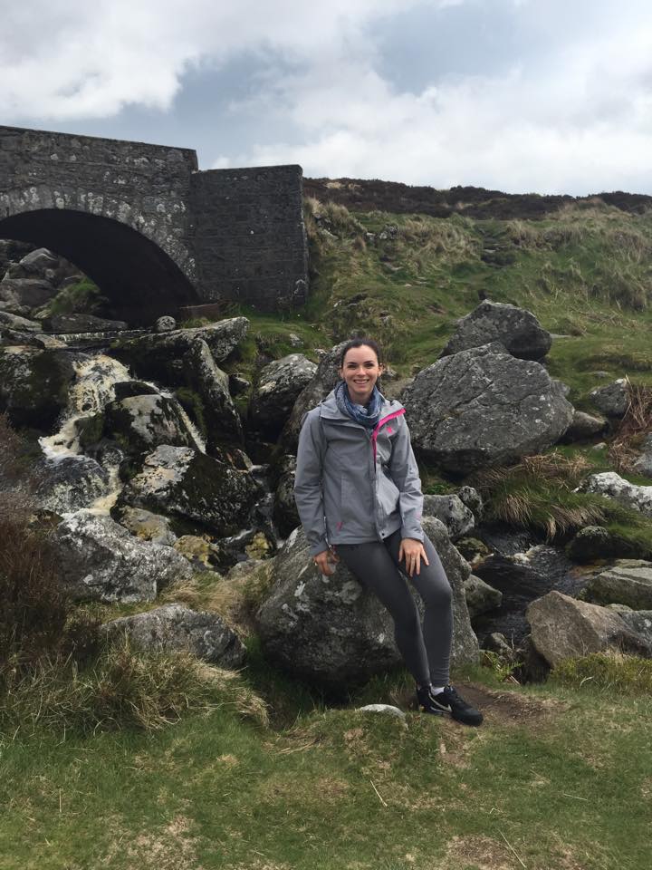 Katie sitting on a rock in front of a bridge on the Sally Gap in Wicklow on a stormy day.