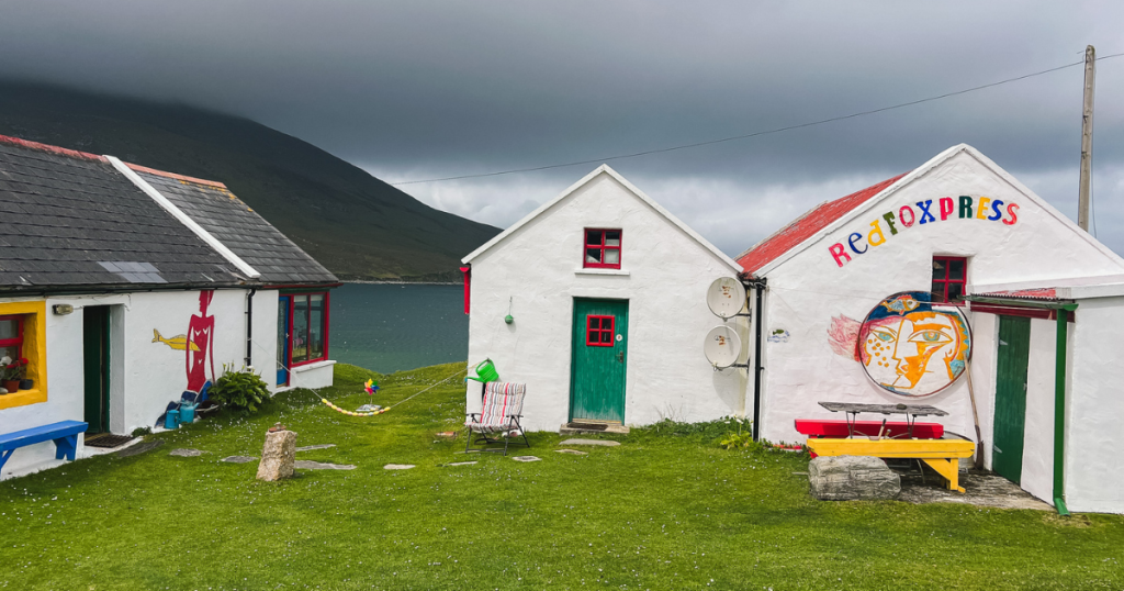 White buildings with colorful doors and words on them overlooking the sea near Dugort Beach in Ireland.