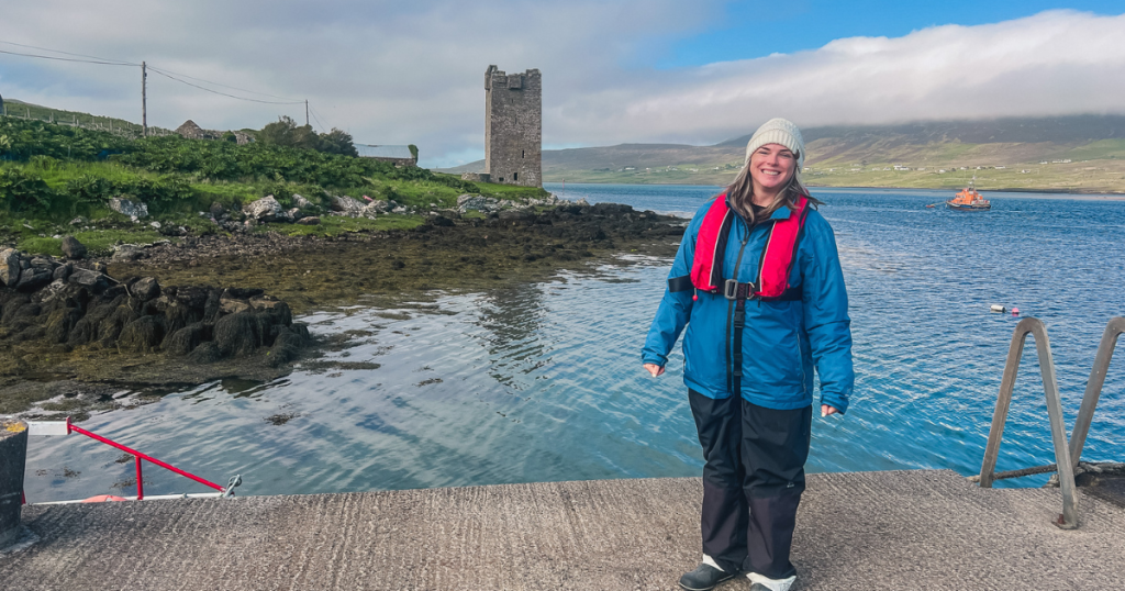 Katie standing on a pier in front of water with a tower castle in the background.