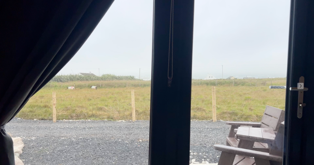View of sheep grazing on a green field out of the door of a glamping pod on Achill Island.
