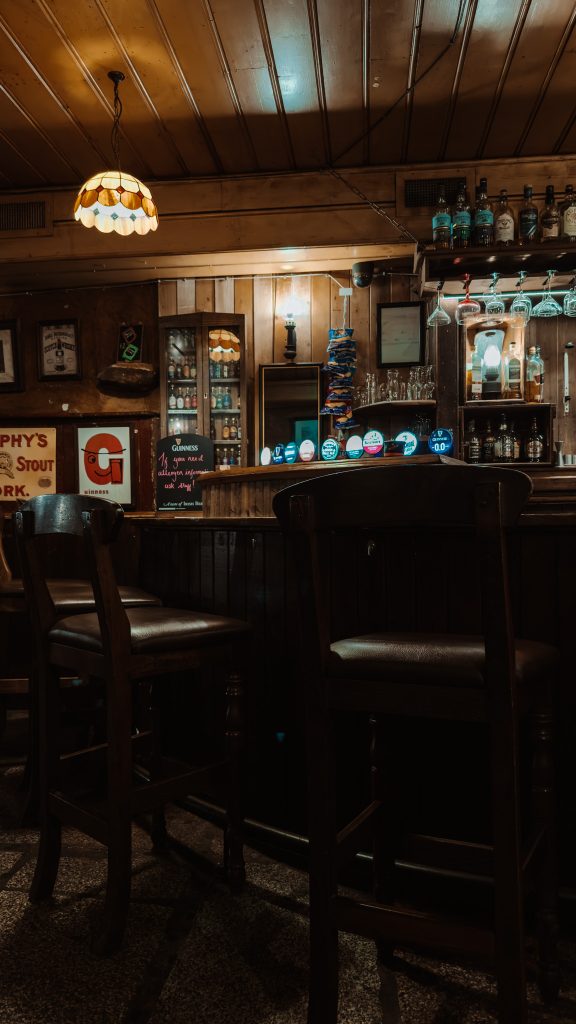 Empty bar chairs next to a bar with beer taps and alcohol bottles on shelves.