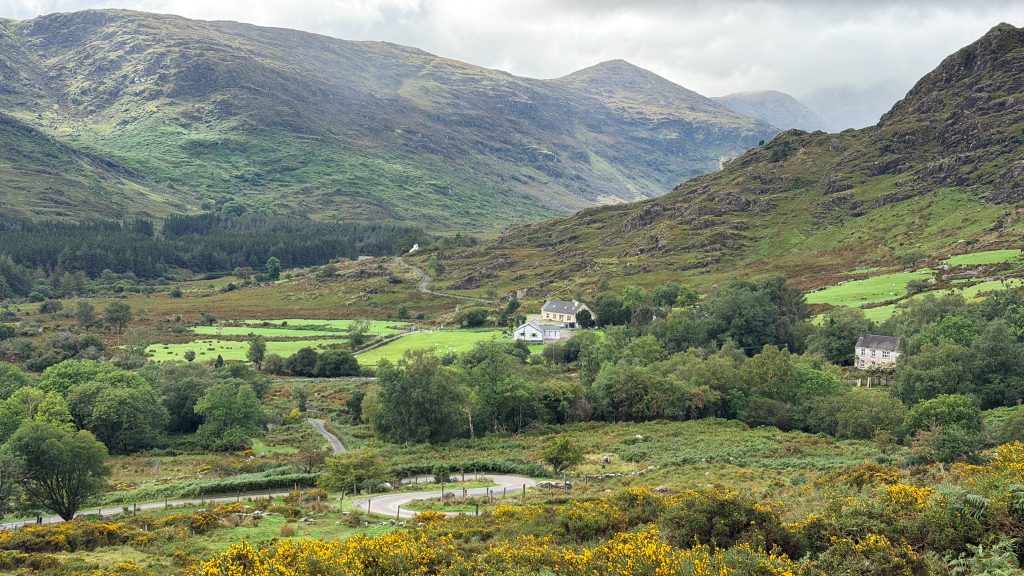 Small houses amidst green farmland beneath rugged mountains in Killarney, Ireland.