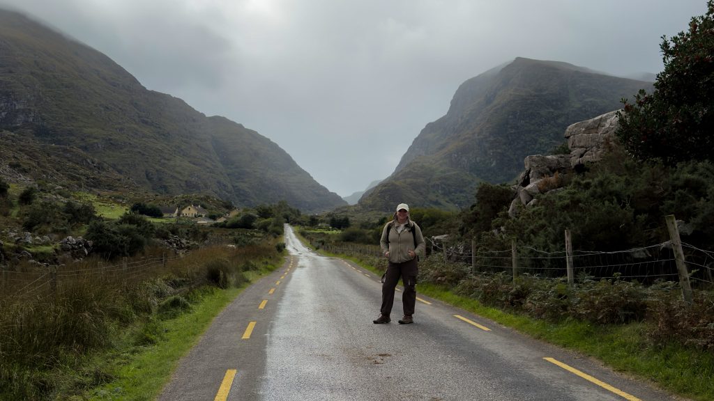 Woman standing on a paved road with mountain peaks in the distance in Ireland.